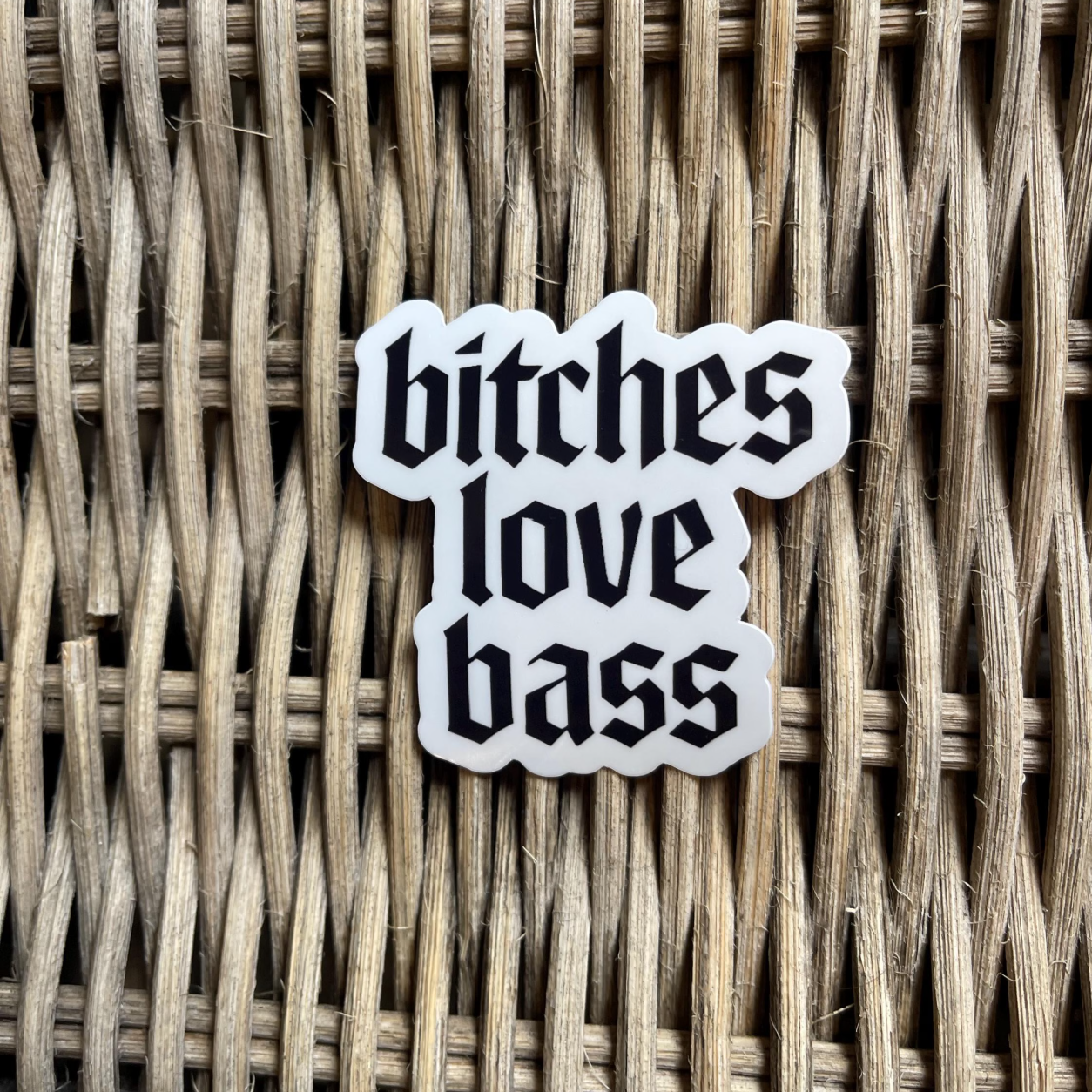 Sticker with 'bitches love bass' text on a woven surface