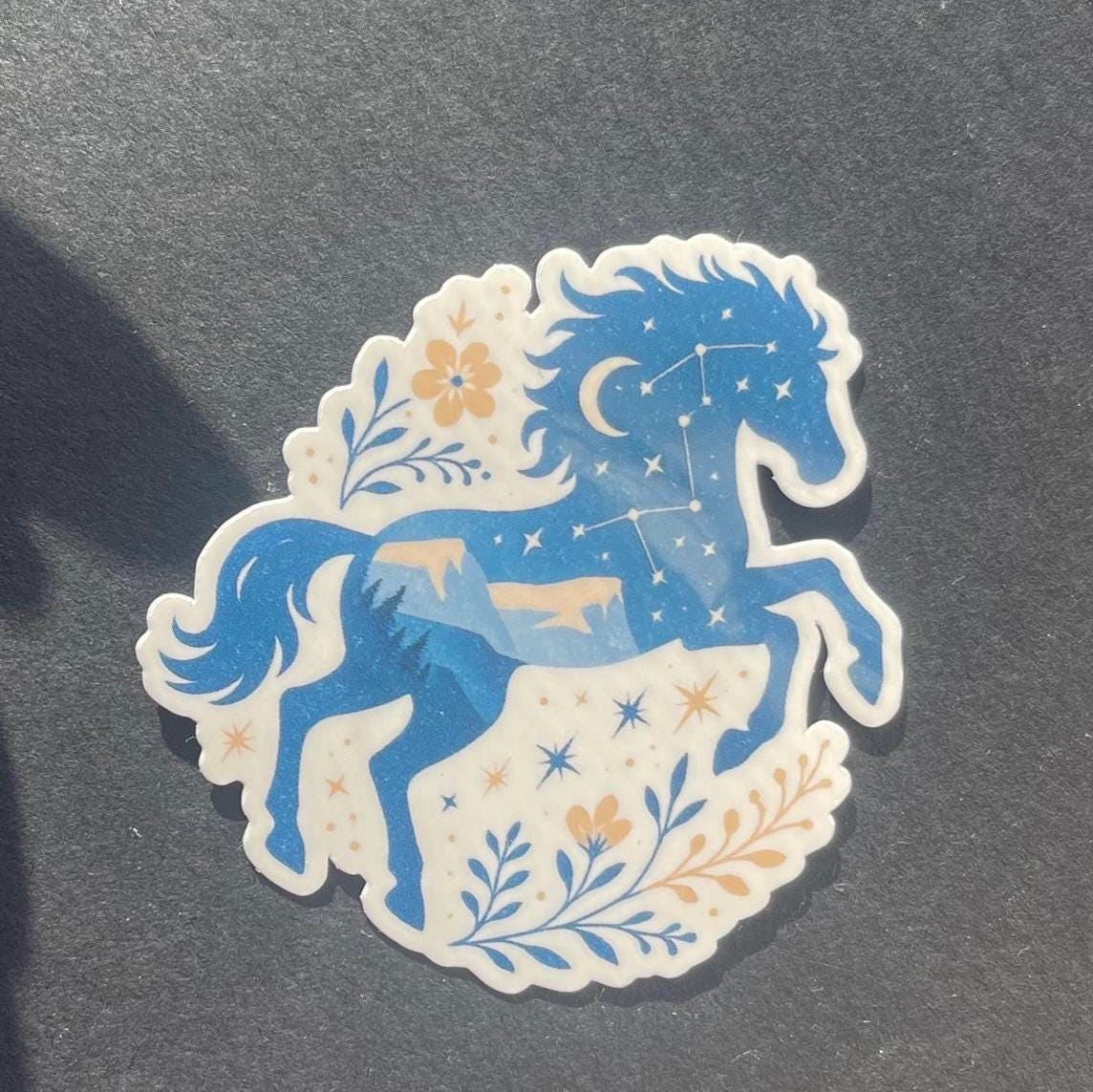 Decorative sticker of a blue horse with floral elements on a dark background