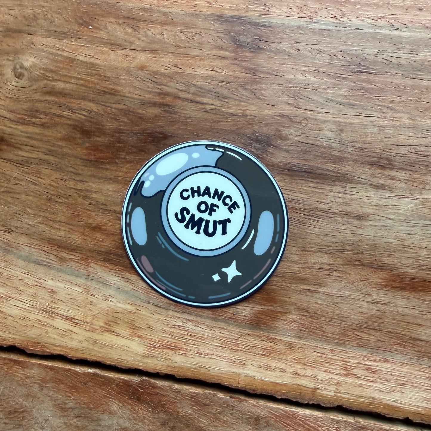 Round sticker with 'Chance of Smut' text on a wooden surface