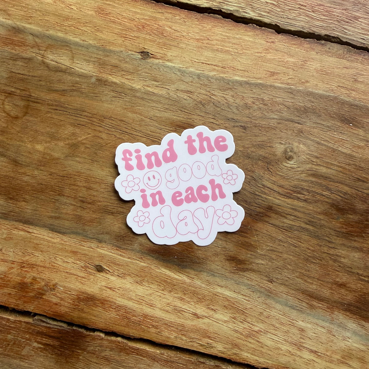 Sticker with 'find the good in each day' text on a wooden surface