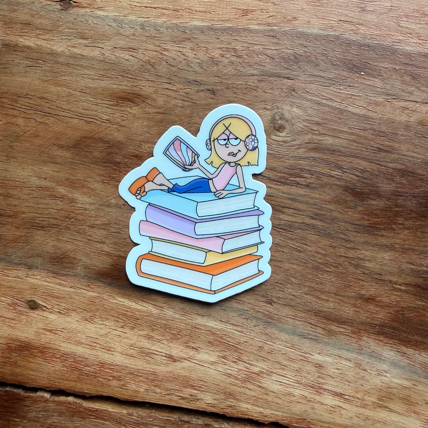 Sticker of a person sitting on books with a book in hand on a wooden surface