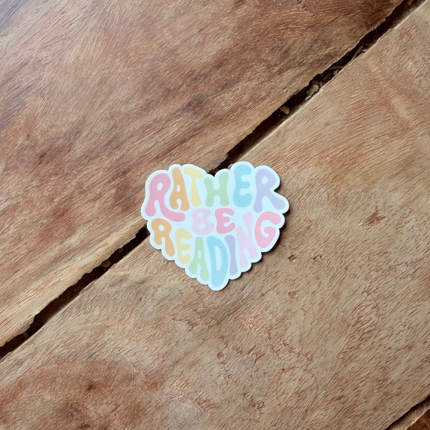 Heart-shaped sticker with 'Rather be reading' text on a wooden surface