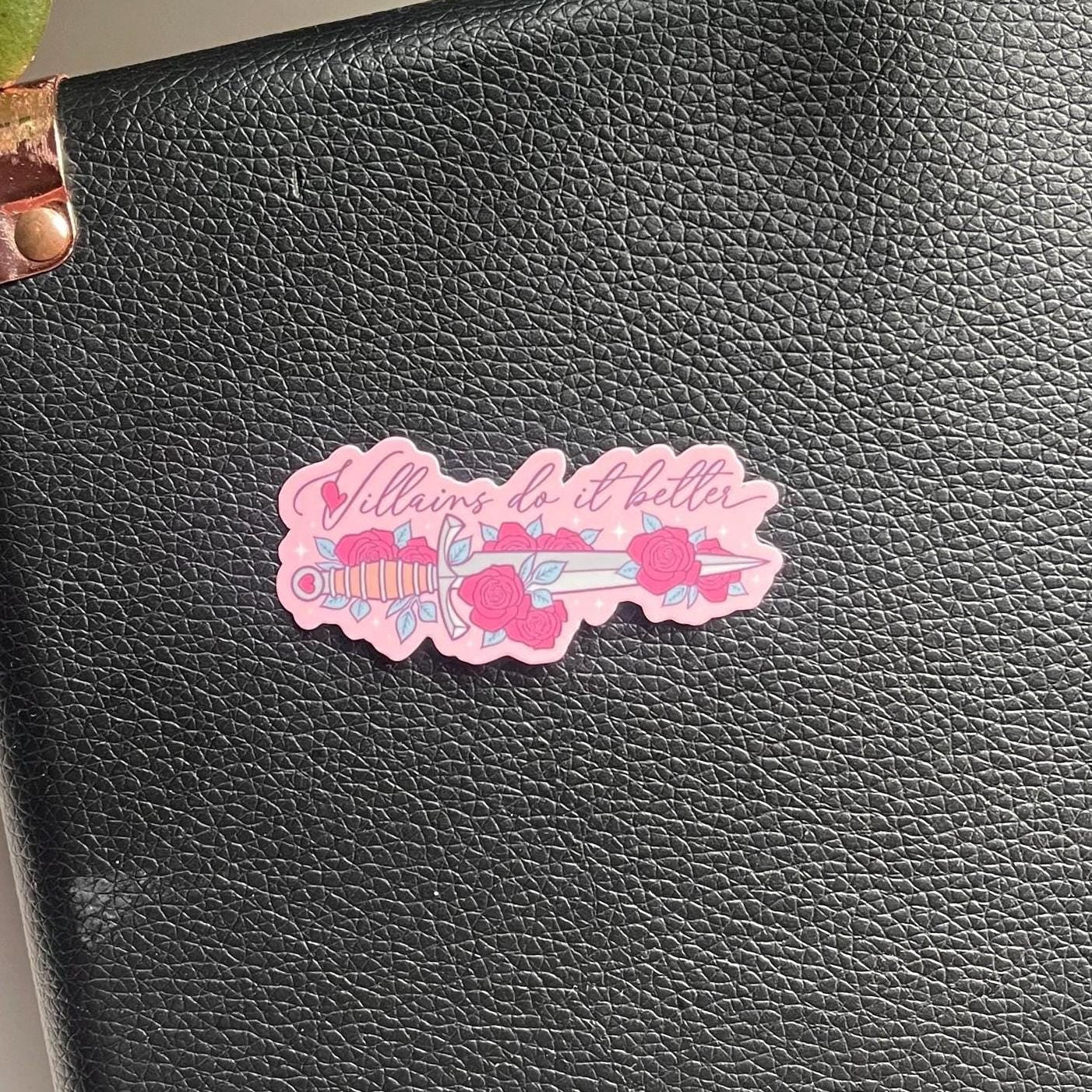 Black leather product with a decorative pink sticker featuring text and floral designs.