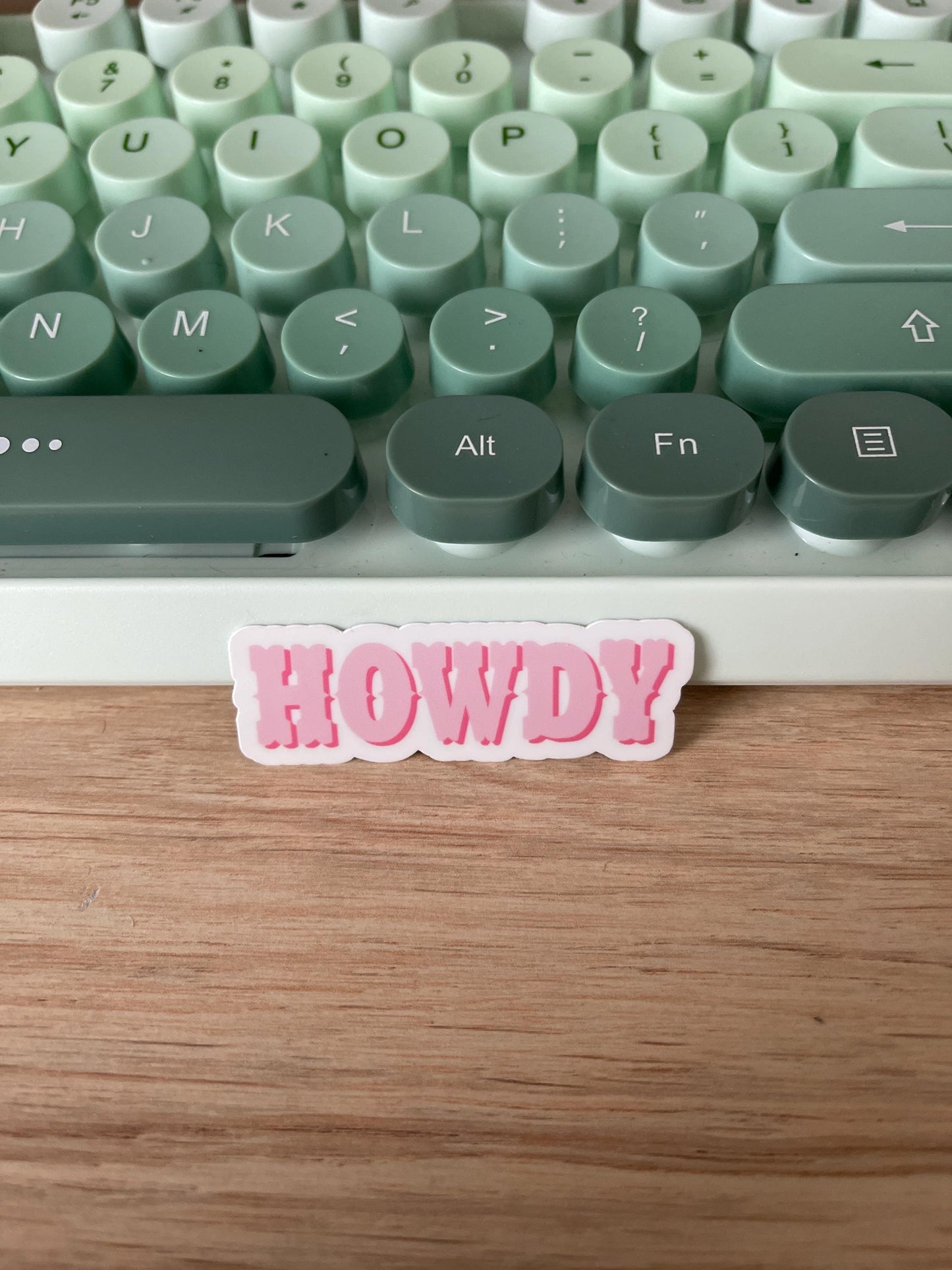 Keyboard with a 'HOWDY' sticker on a wooden surface