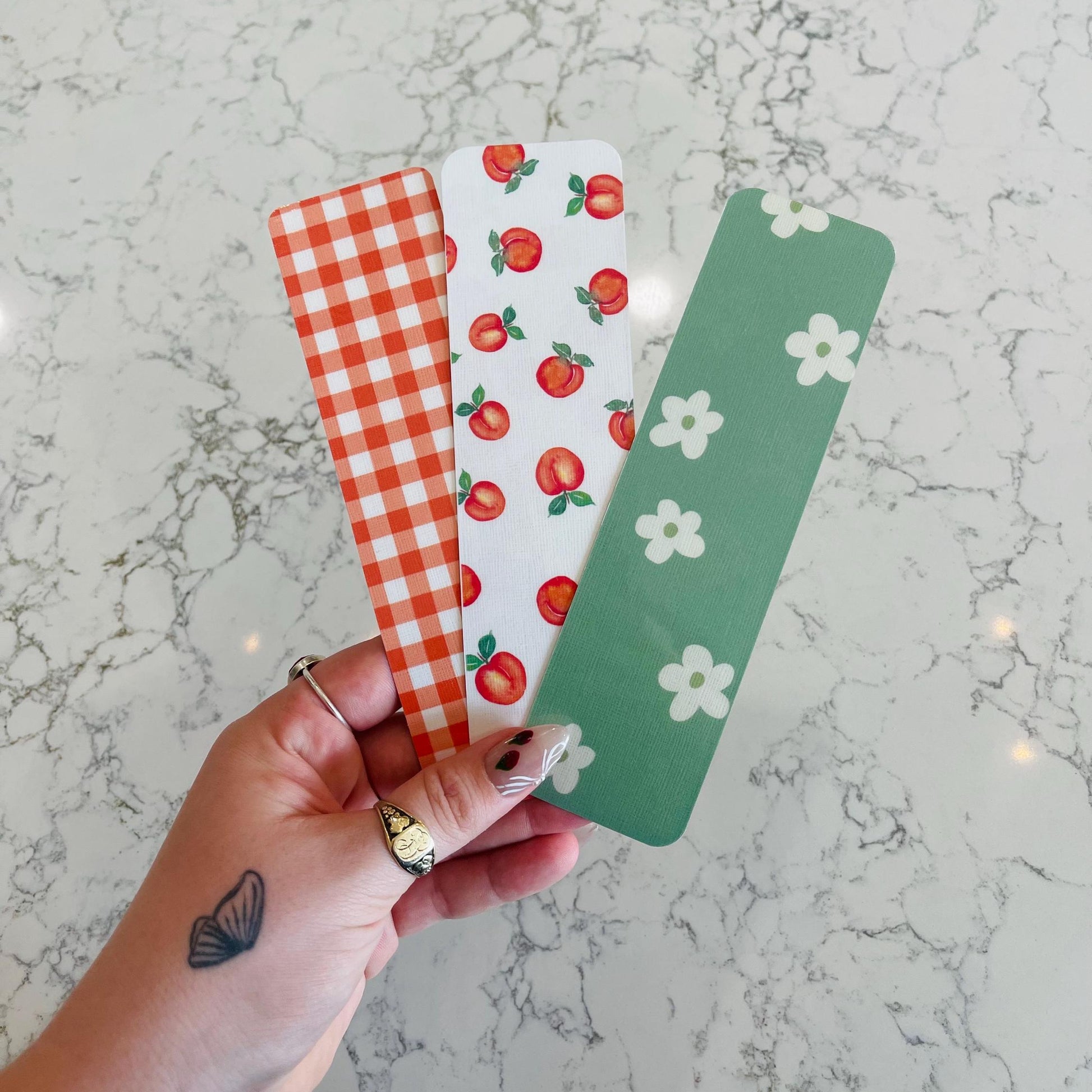 Three colorful bookmarks with different patterns held by a hand on a marble surface.