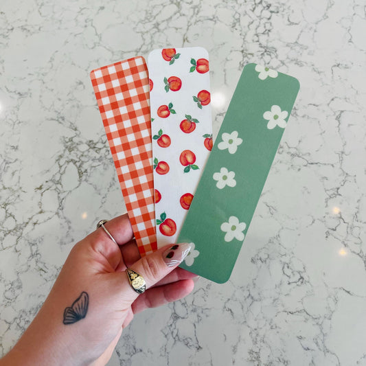Three colorful bookmarks with different patterns held by a hand on a marble surface.