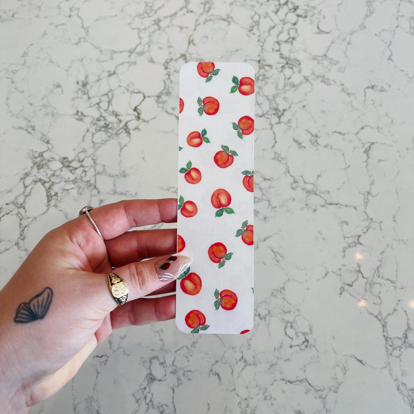 White bookmark with peaches held over a marble surface