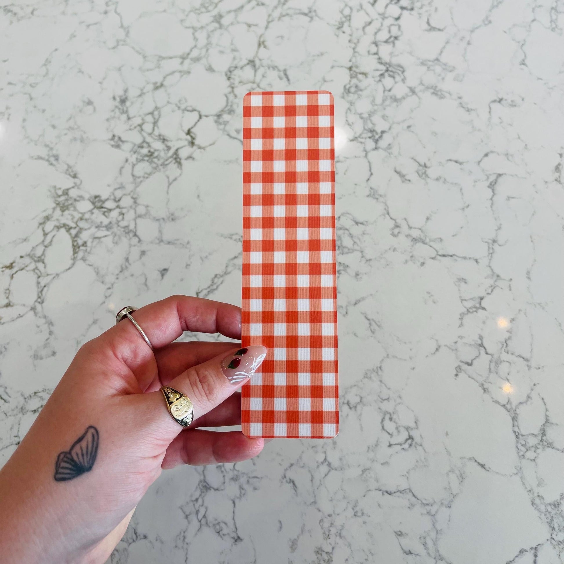 Hand holding an orange and white gingham bookmark against a marble background