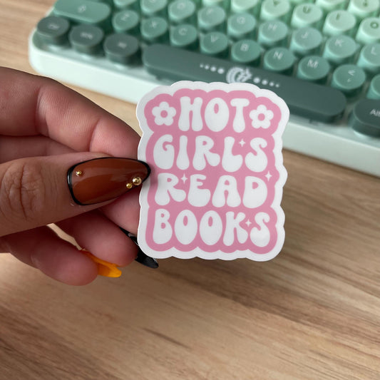 Hand holding a pink sticker with 'Hot Girls Read Books' text in front of a green keyboard.