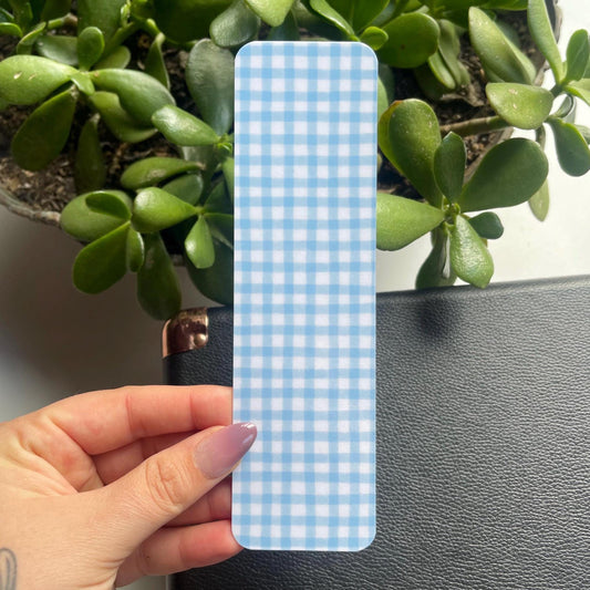 Blue and white checkered phone case held by a hand with green plants in the background