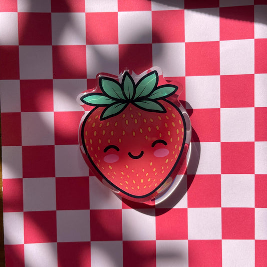 Strawberry-shaped phone grip with a smiley face on a red and white checkered background