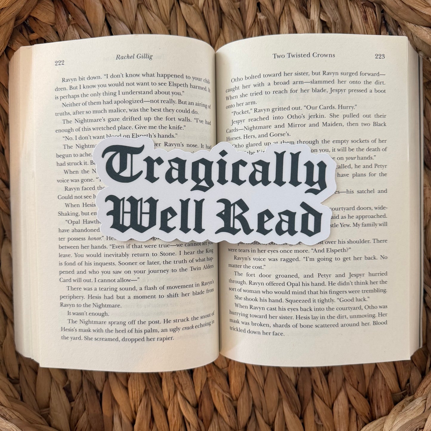Open book with 'Tragically Well Read' text bookmark overlay on a woven surface