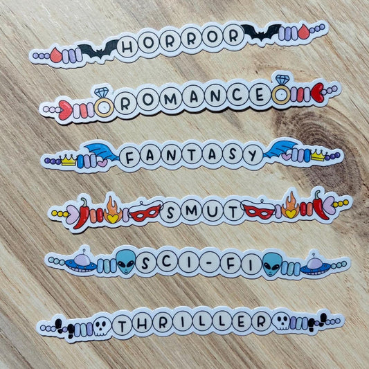 Stickers labeled 'Horror', 'Romance', 'Fantasy', 'Smut', 'Sci-Fi', and 'Thriller' on a wooden surface.
