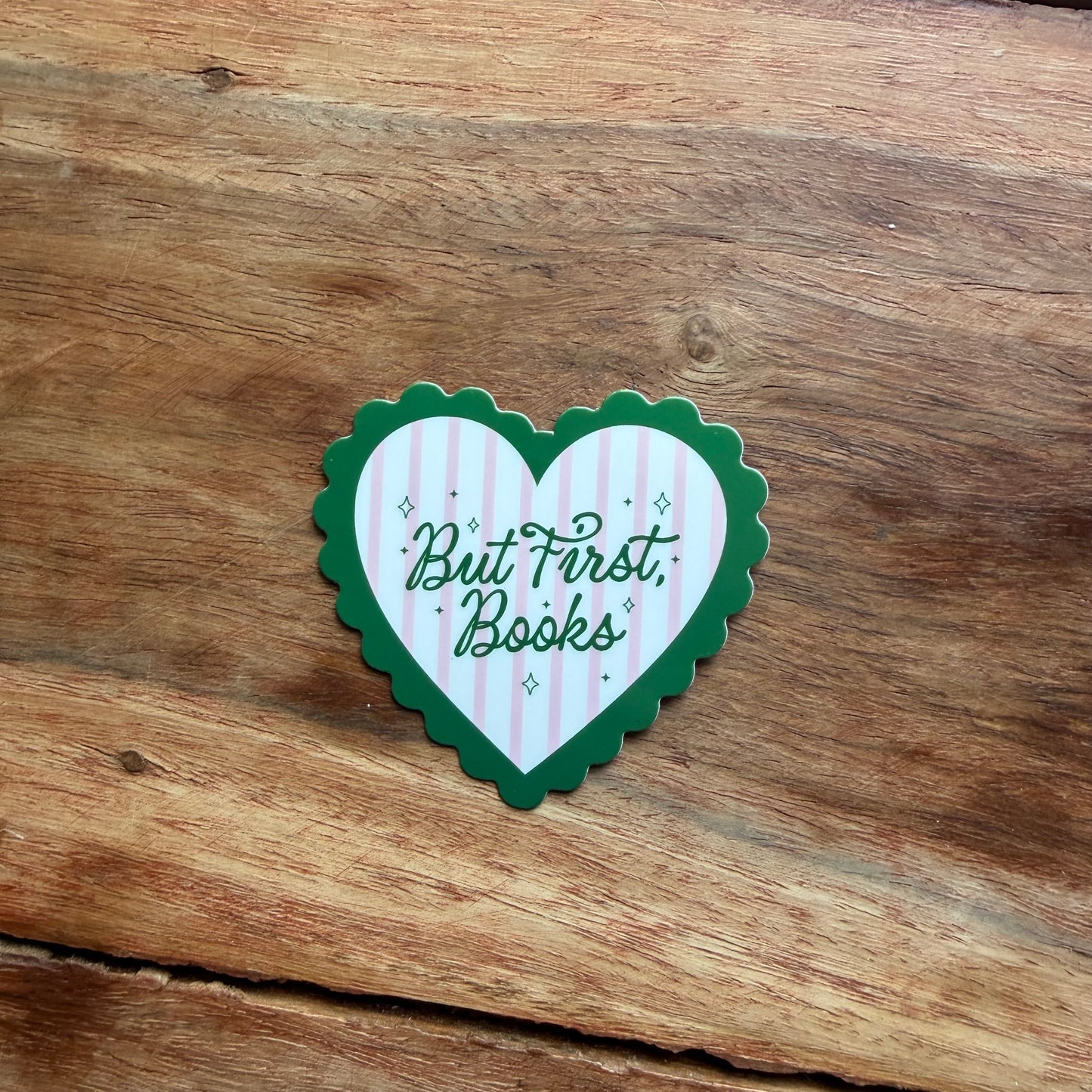 Heart-shaped sticker with 'But First, Books' text on a wooden surface