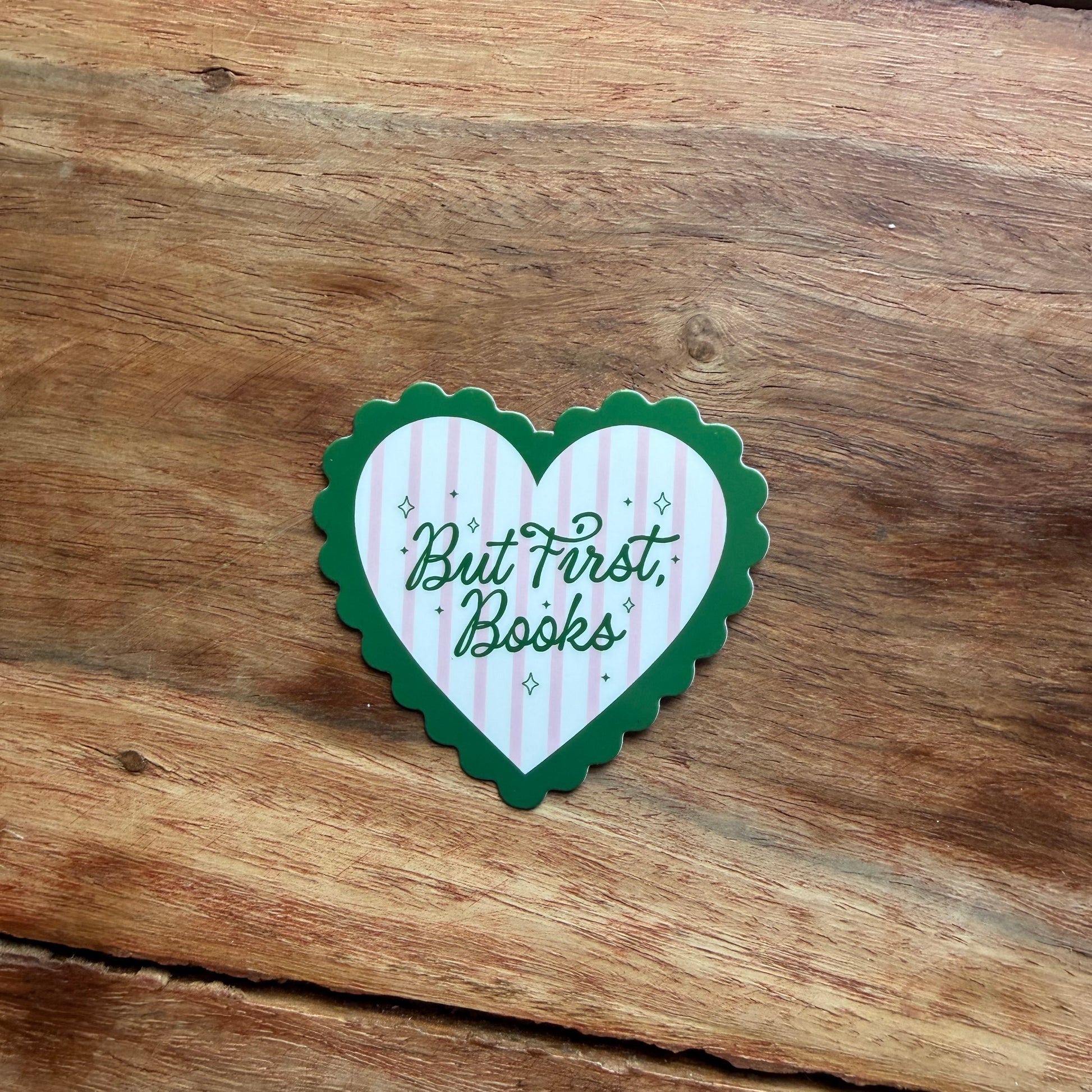 Heart-shaped sticker with 'But First, Books' text on a wooden surface