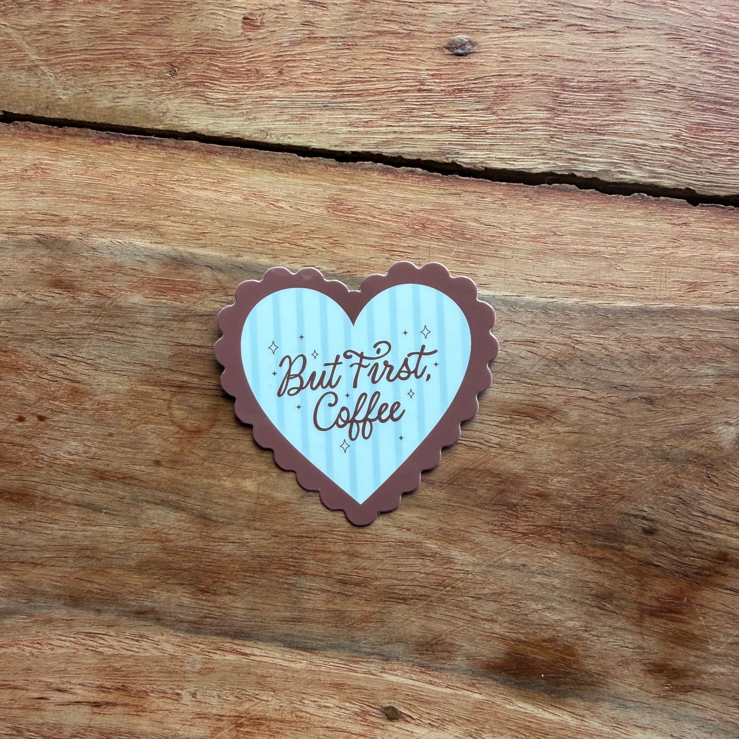 Heart-shaped sticker with 'But First, Coffee' text on a wooden surface