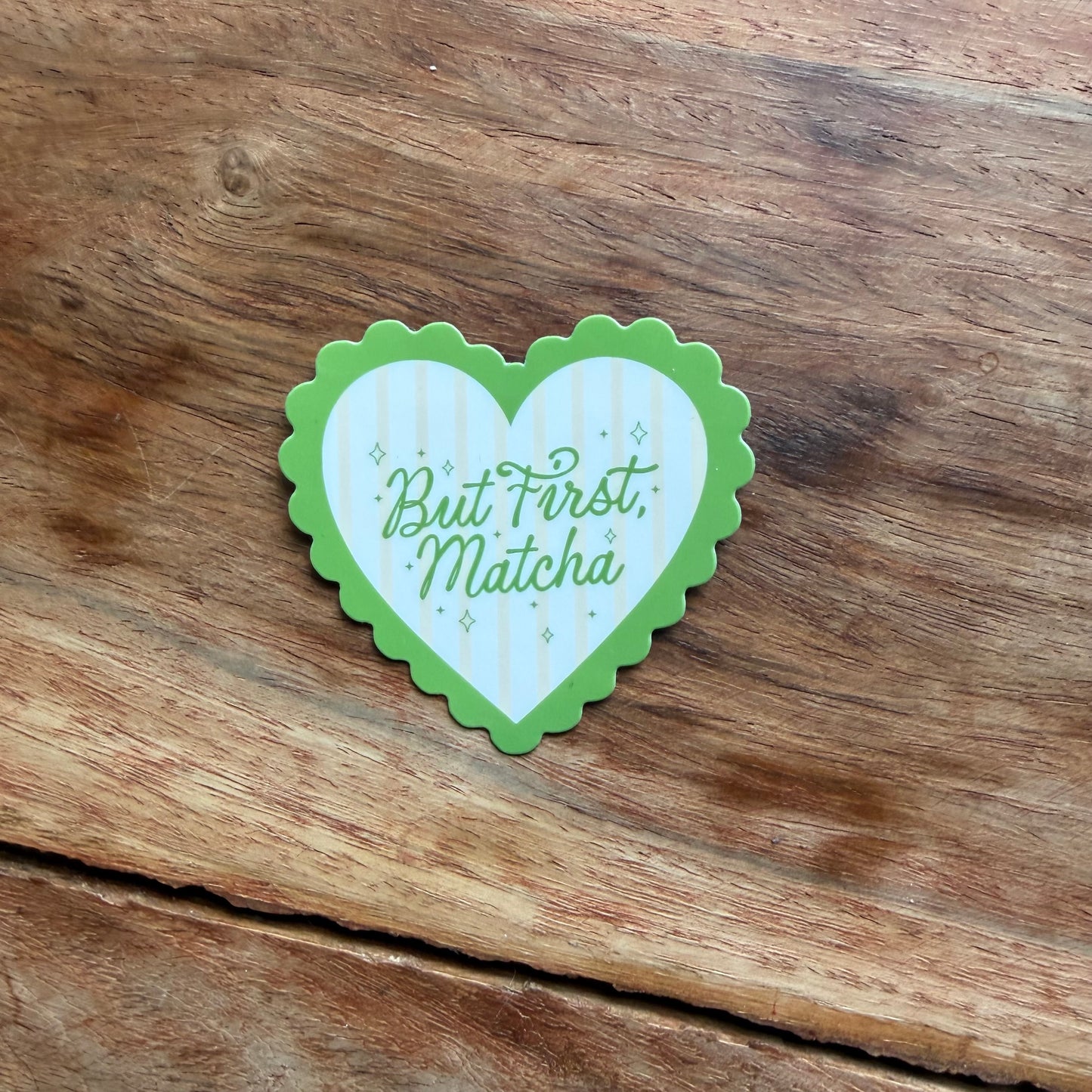 Heart-shaped sticker with 'But First, Matcha' text on a wooden surface