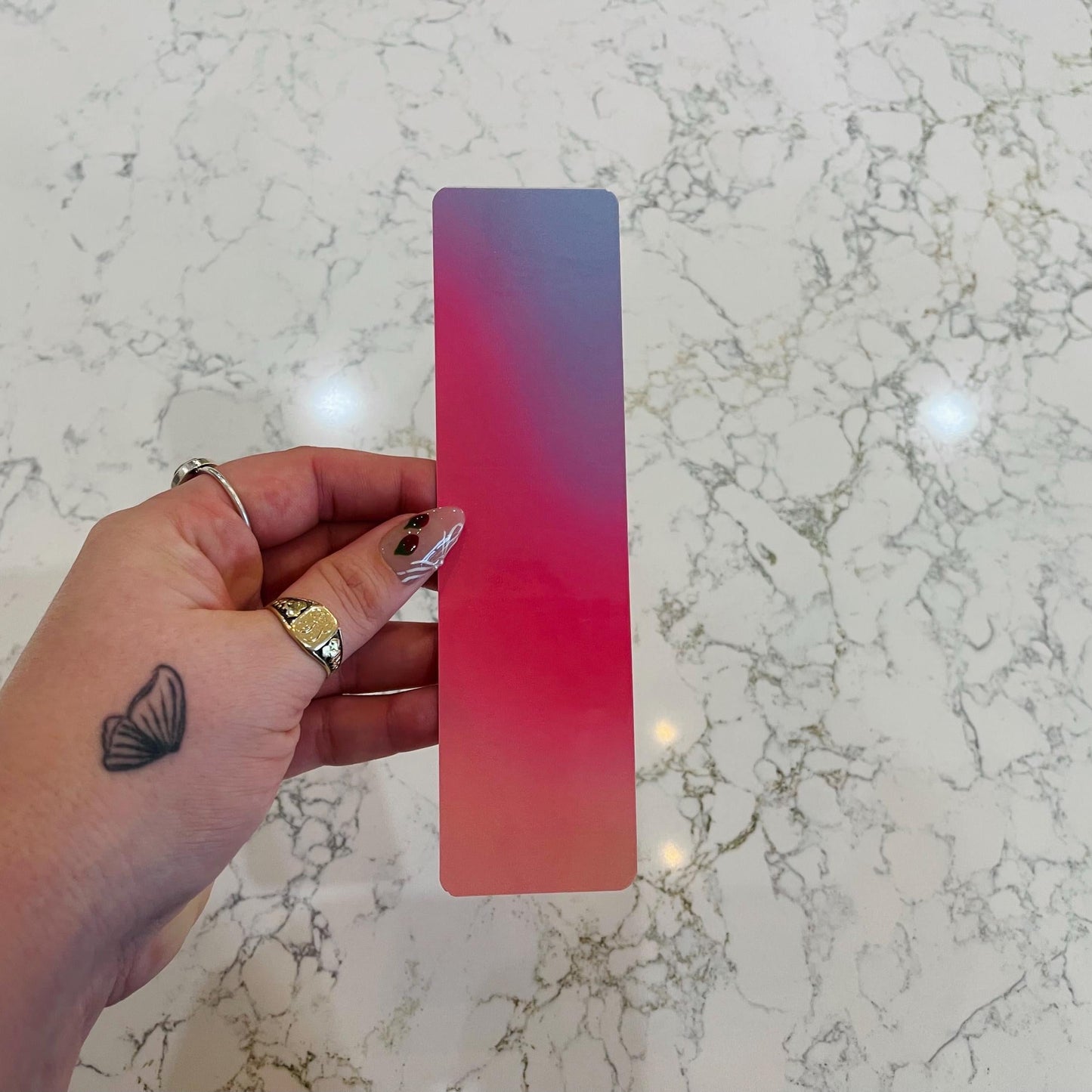 Hand holding a pink to blue gradient bookmark on a marble surface