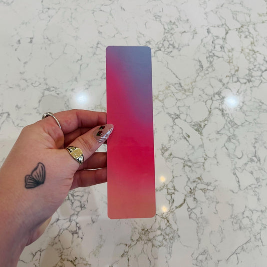 Hand holding a pink to blue gradient bookmark on a marble surface