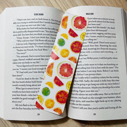 Open book with colorful fruit-themed bookmark on a wooden surface