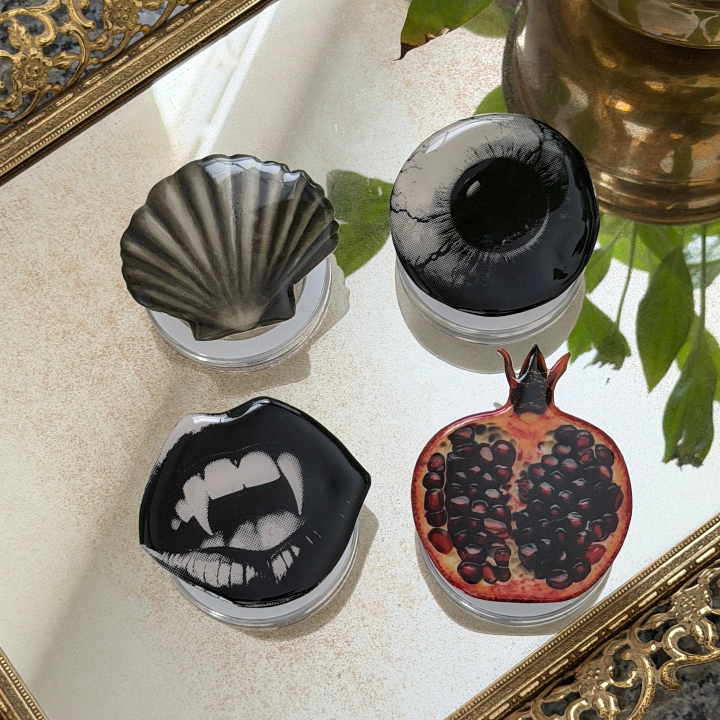 Decorative phone grips with artistic designs on a mirror surface with potted plants.