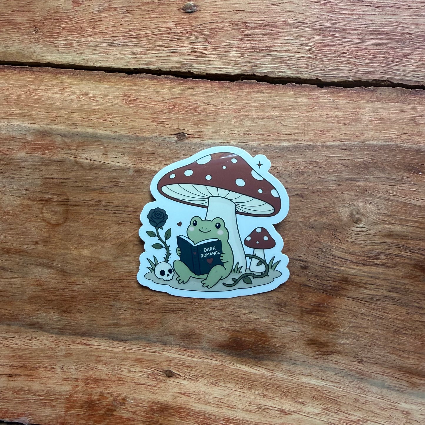 Sticker of a frog under a mushroom on a wooden surface