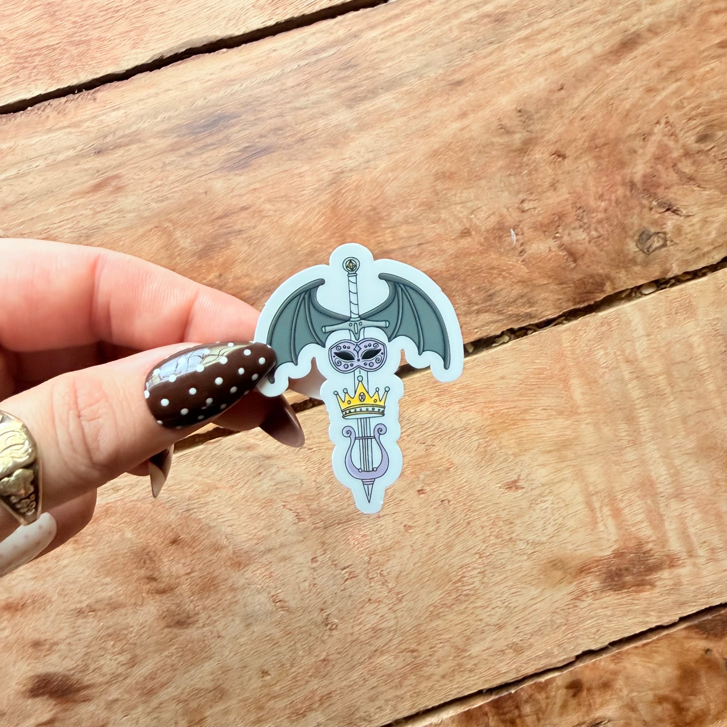 Hand holding a decorative sticker with a bat design on a wooden surface