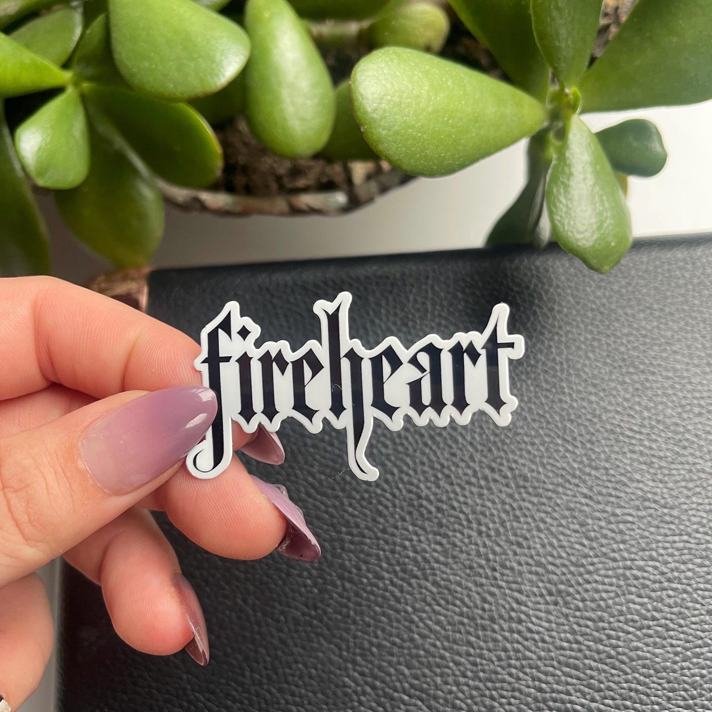 Hand holding a 'fireheart' sticker with a green plant in the background