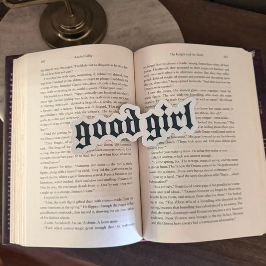 Open book with a 'good girl' bookmark on a wooden surface