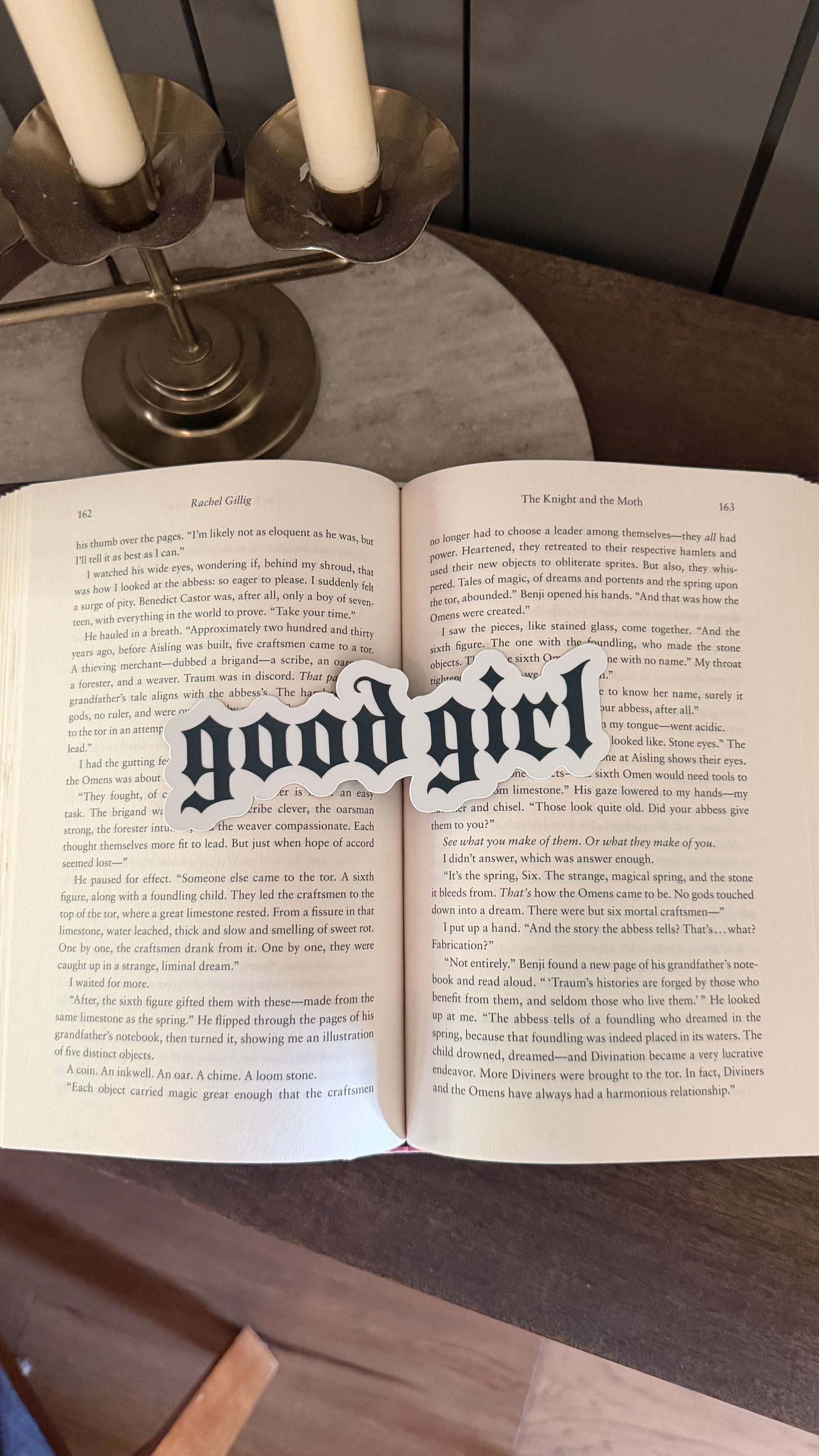 Open book with a bookmark reading 'good girl' on a wooden surface.