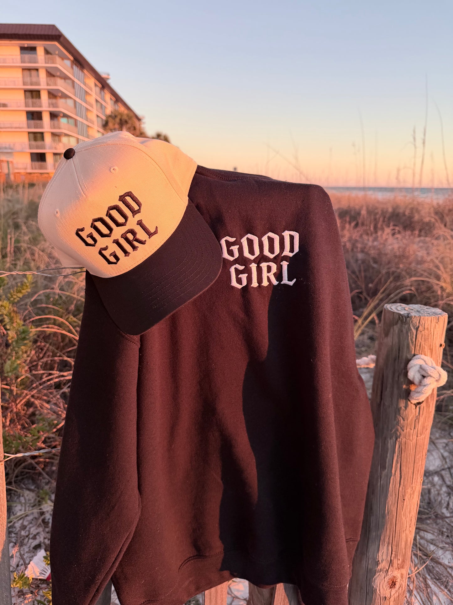 black sweatshirt and white cap with 'GOOD GIRL' text against a blurred outdoor background