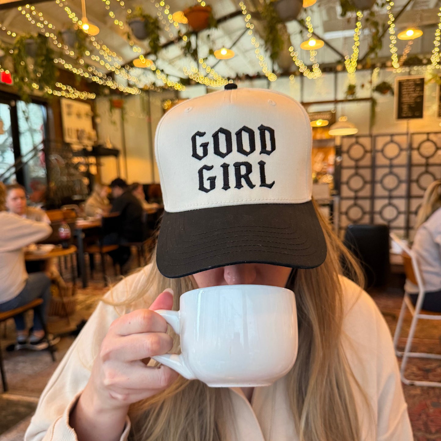 person drinking coffee wearing a good girl embroidered baseball cap