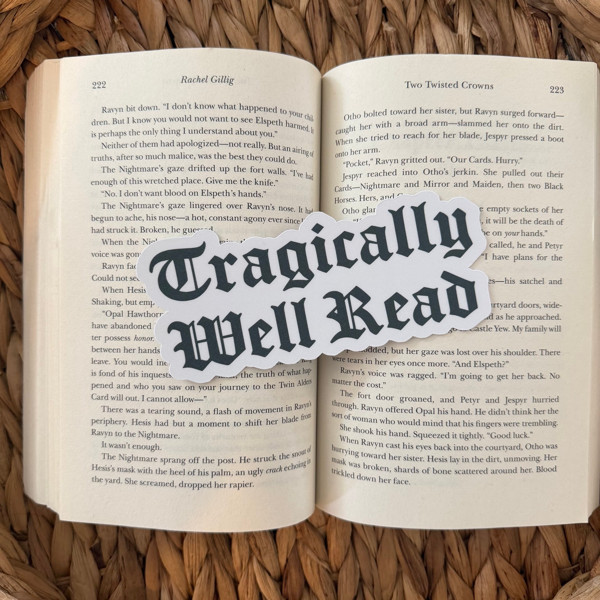 Open book with 'Tragically Well Read' text bookmark overlay on a woven surface