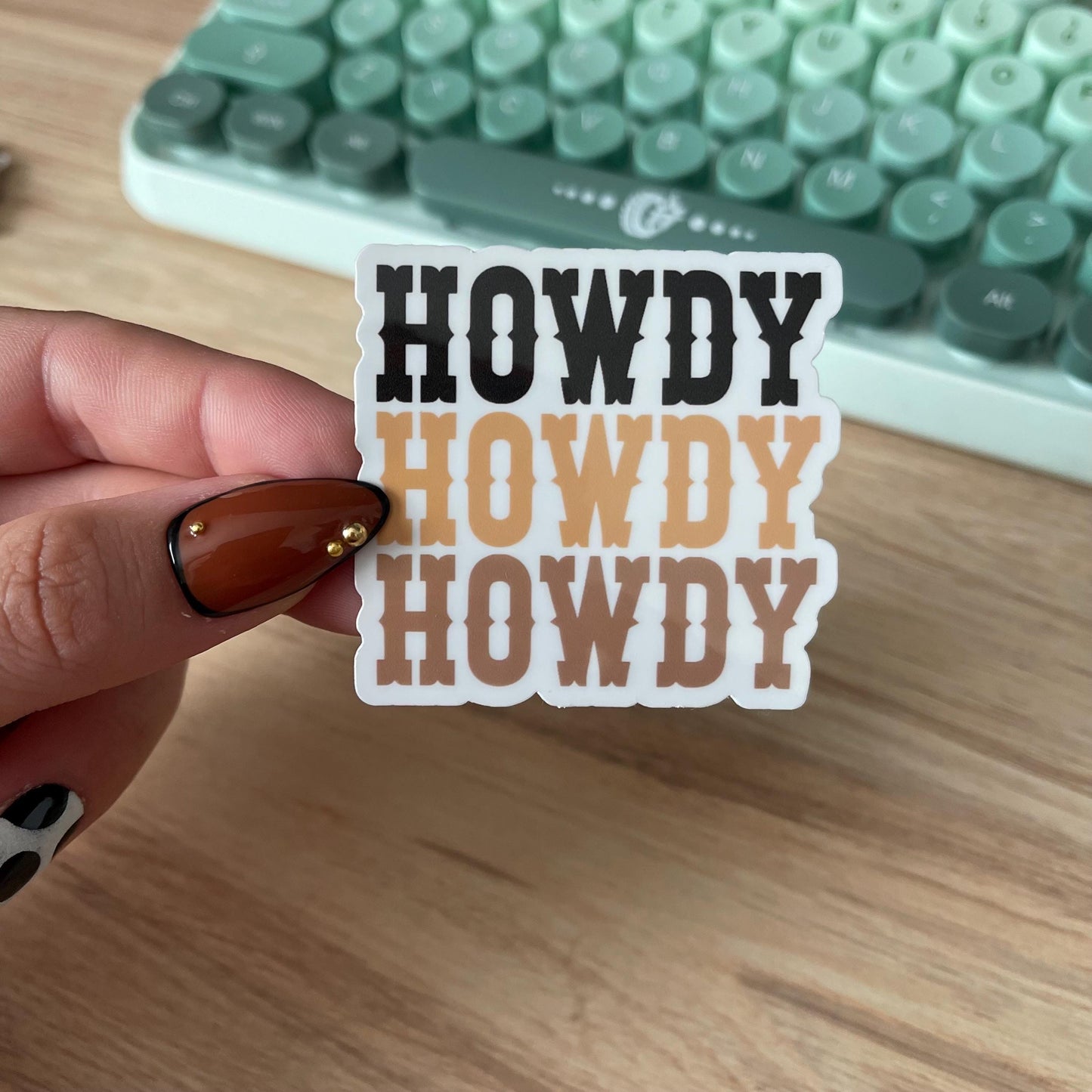 Hand holding a 'HOWDY HOWDY HOWDY' sticker with a vintage typewriter in the background.