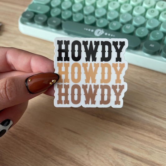 Hand holding a 'HOWDY HOWDY HOWDY' sticker with a vintage typewriter in the background.