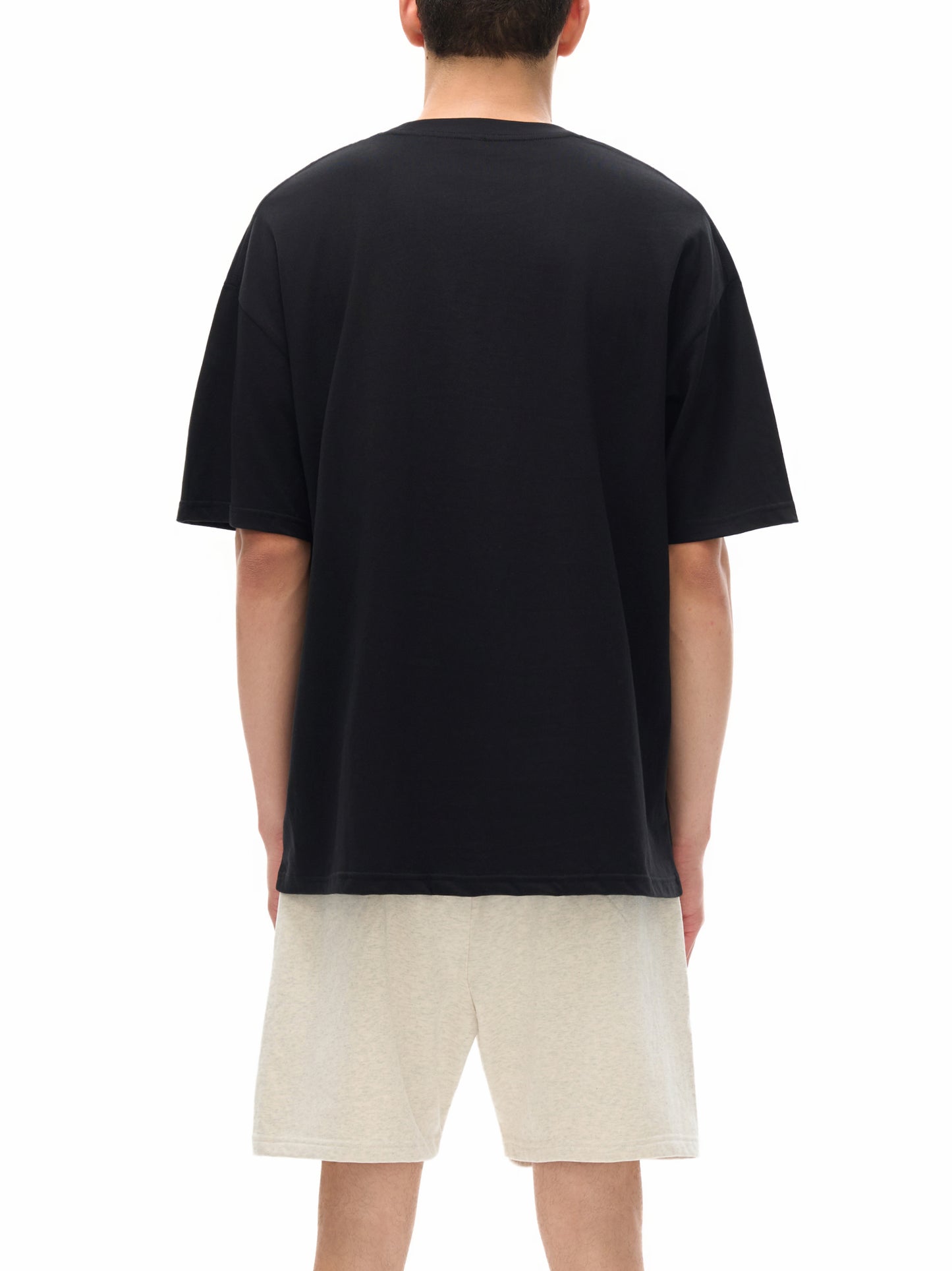 Person wearing a black t-shirt and beige shorts on a white background
