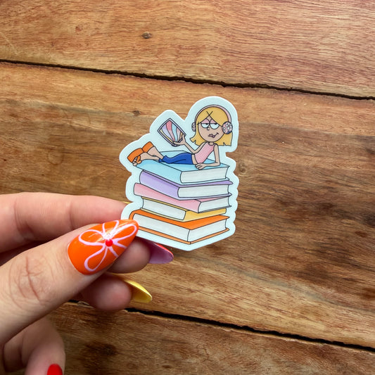 Sticker of a person sitting on books held by a hand with orange nail polish on a wooden surface