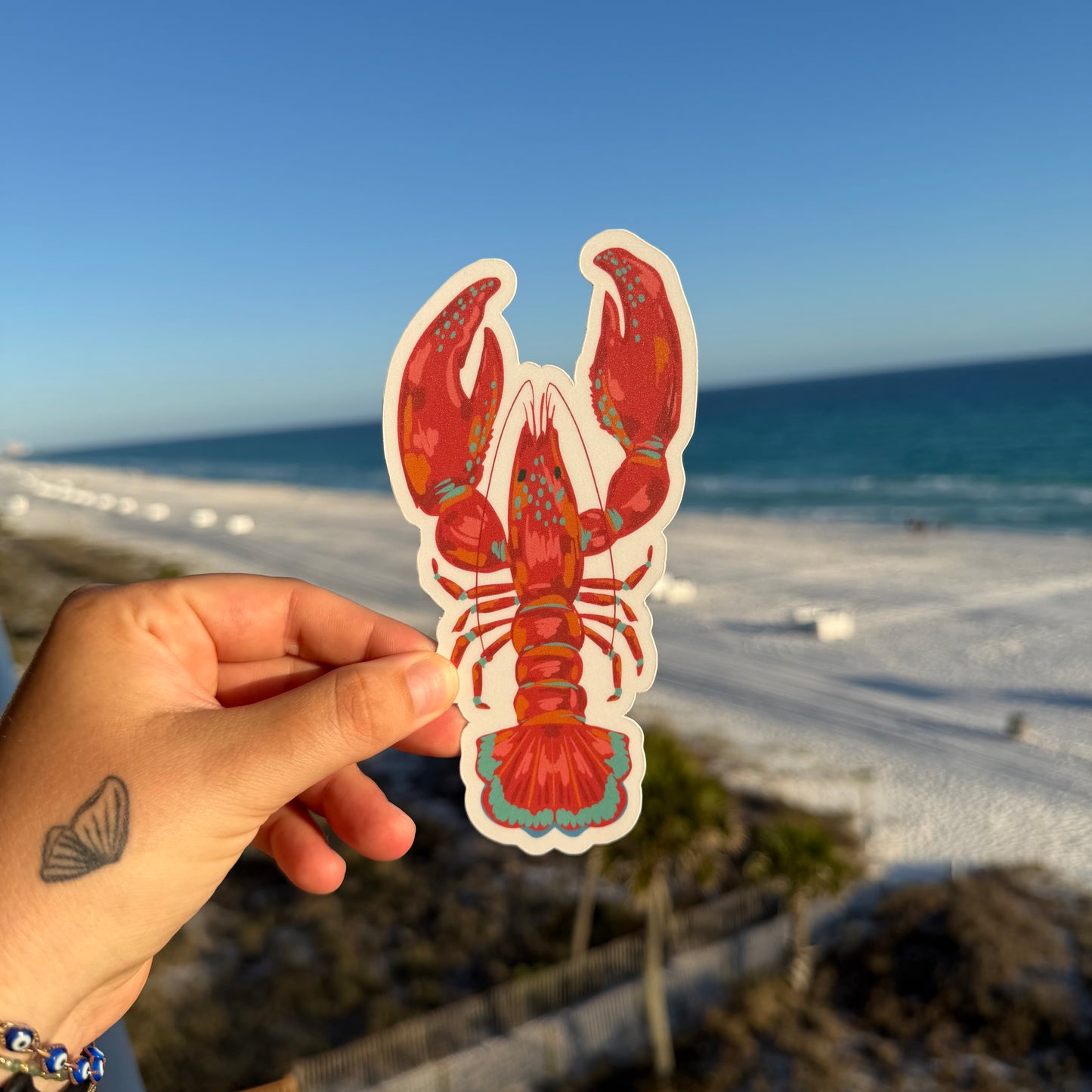 hand holding a lobster shaped bookmark against a beach background