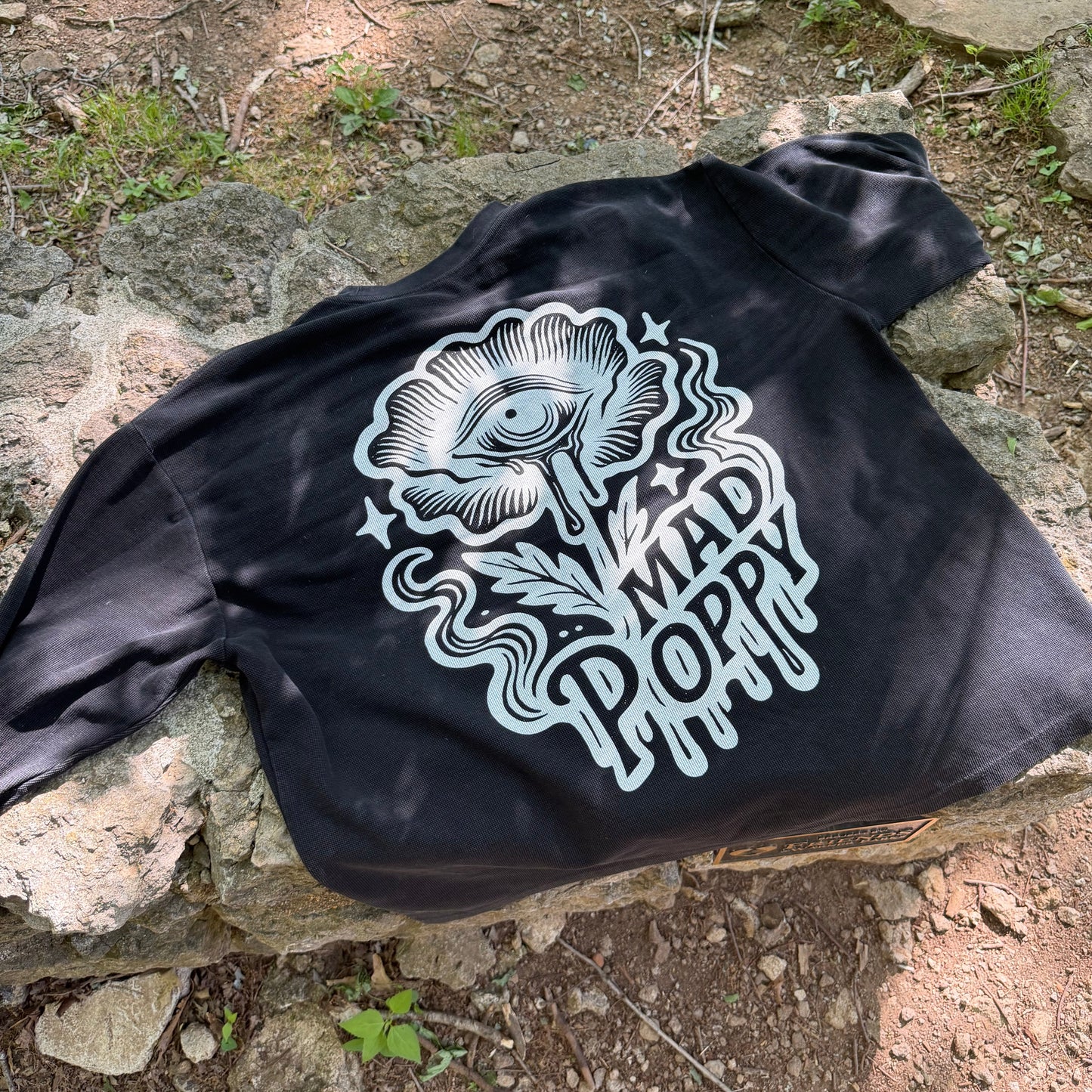 a black long sleeve tshirt with a flower graphic that says 'mad poppy' laying on a stone