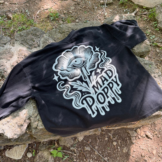 a black long sleeve tshirt with a flower graphic that says 'mad poppy' laying on a stone