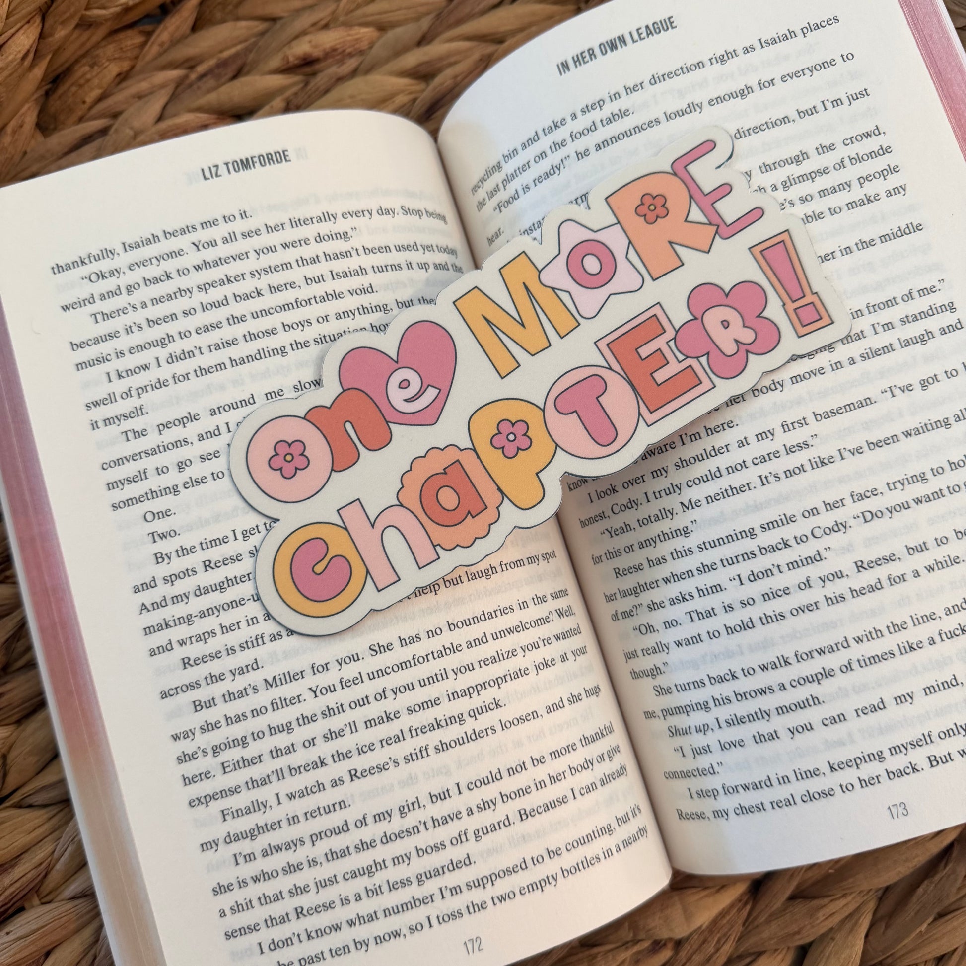 Open book with a colorful bookmark reading 'One More Chapter!' on a woven surface.