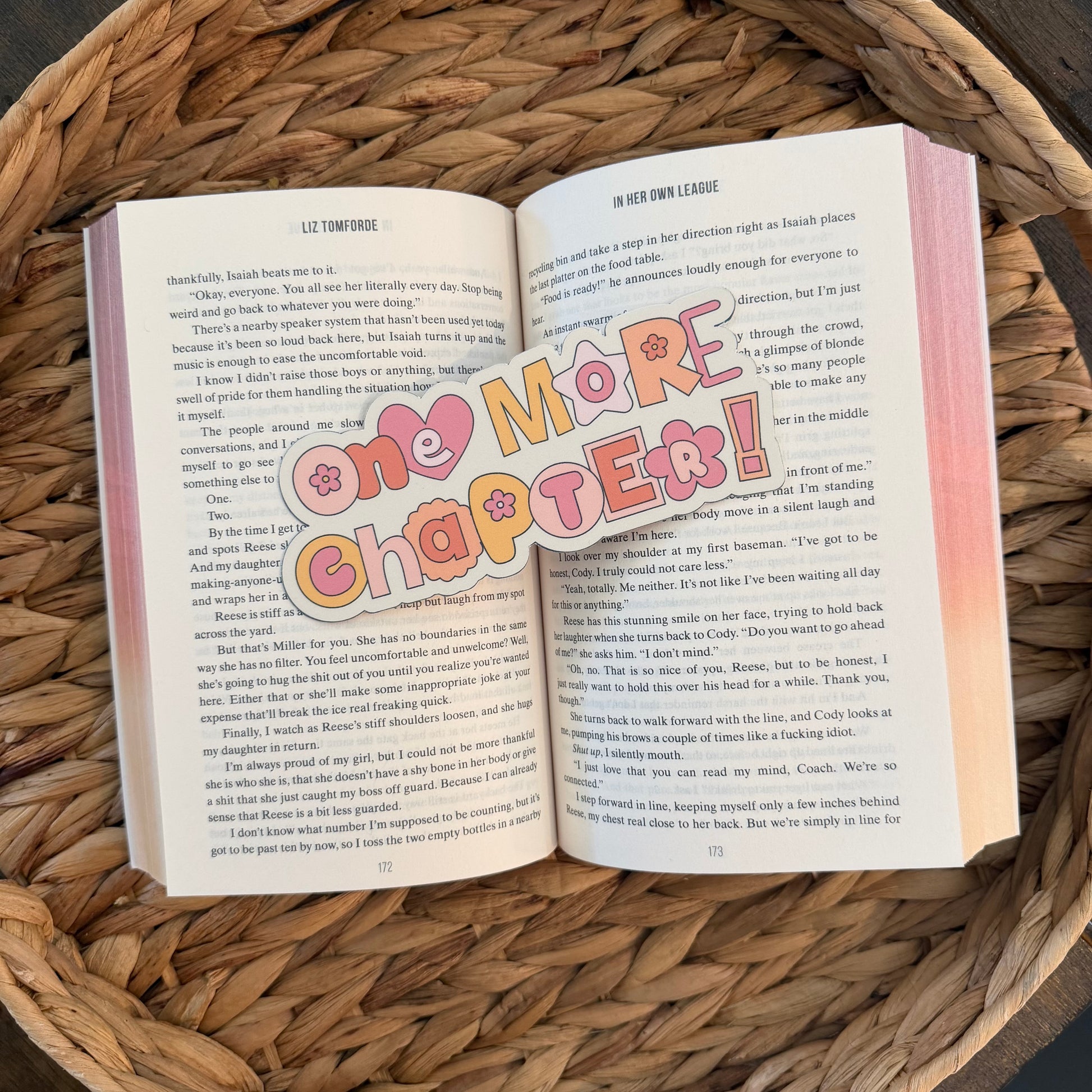 book open with a bookmark that reads "one more chapter" on a woven surface