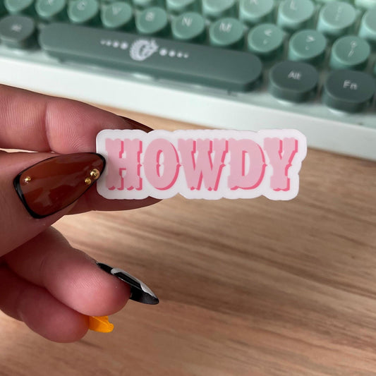 Hand holding a pink 'HOWDY' sticker in front of a typewriter