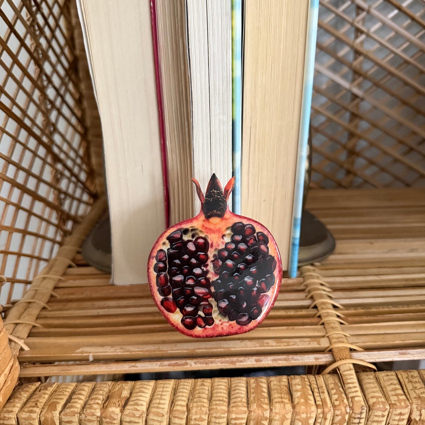 Pomegranate cut in half phone grip on a woven surface with books in the background