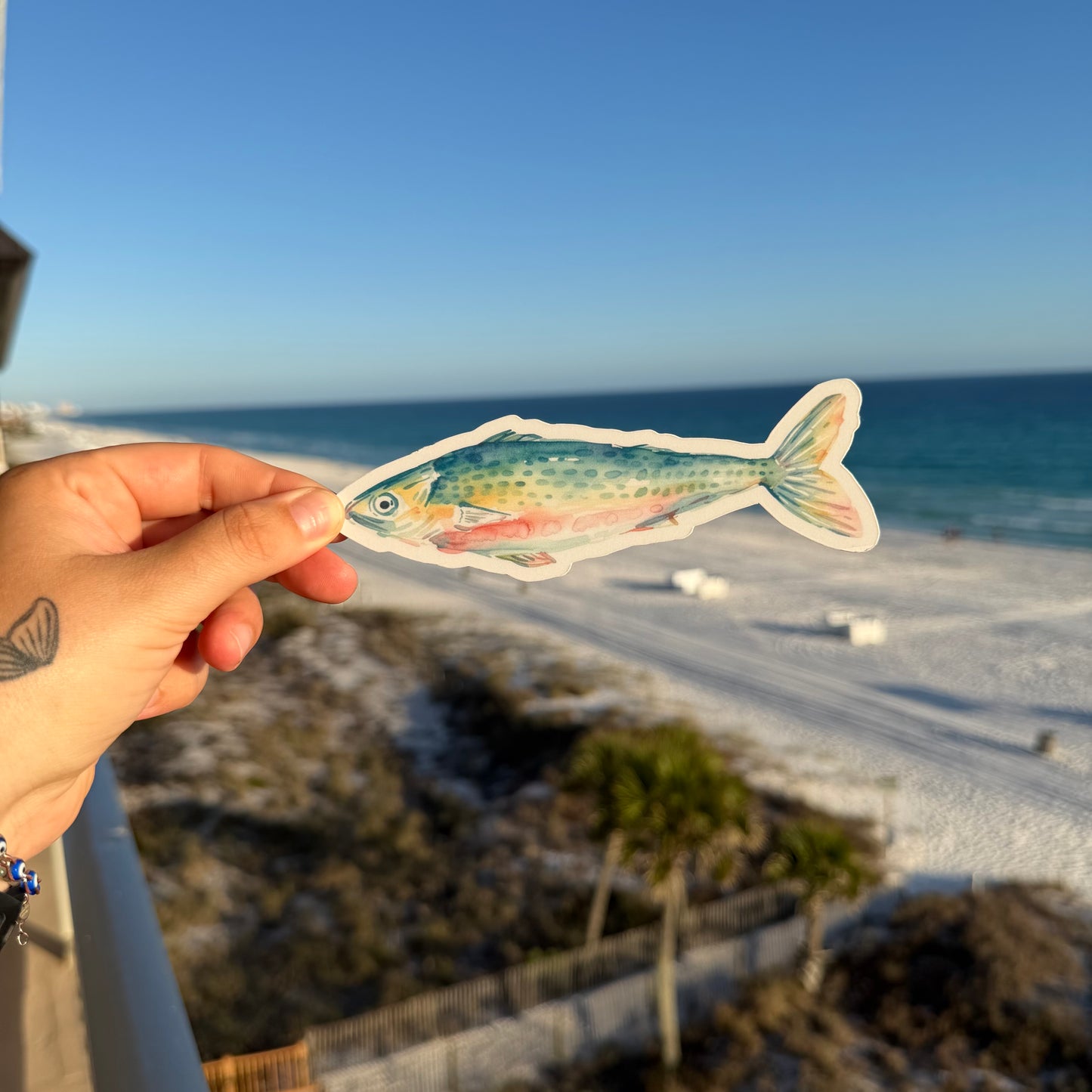 hand holding a sardine shaped bookmark against a beach background