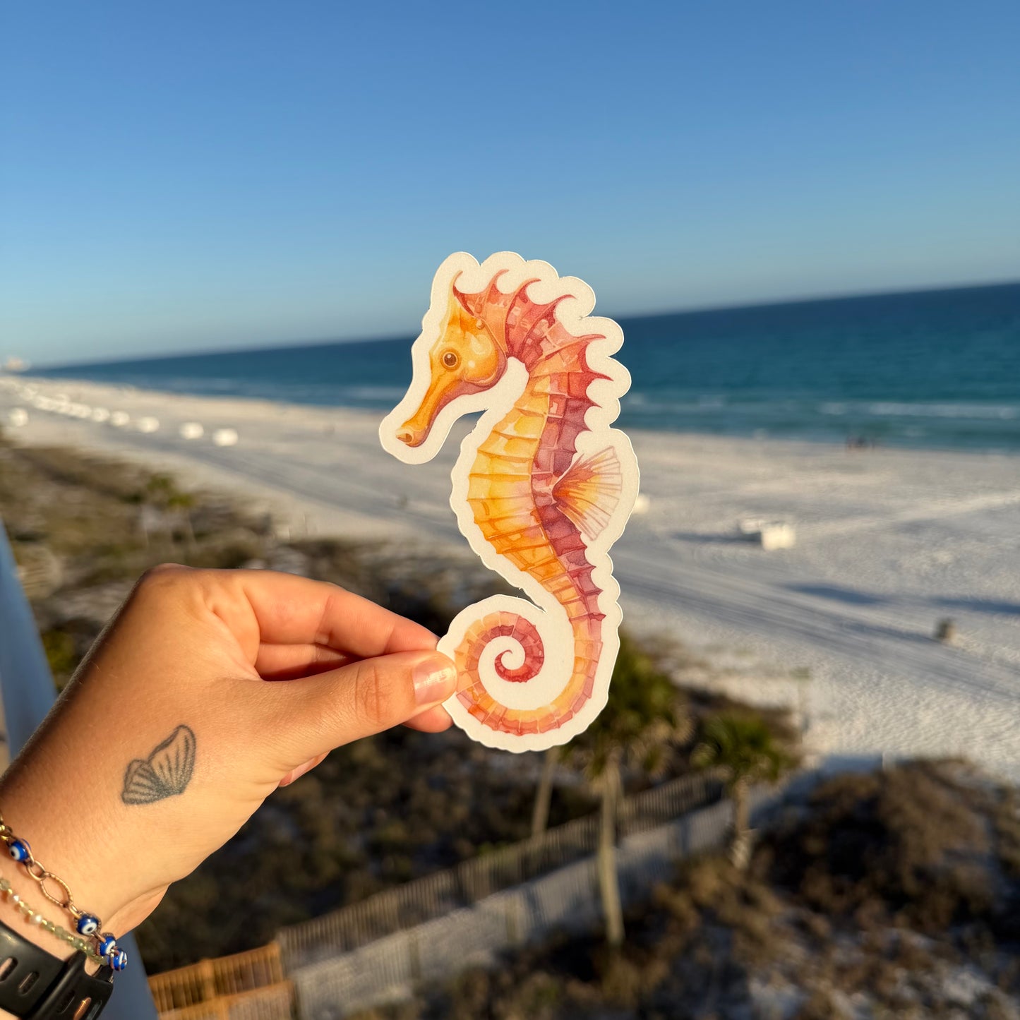hand holding a sea horse shaped bookmark against a beach background