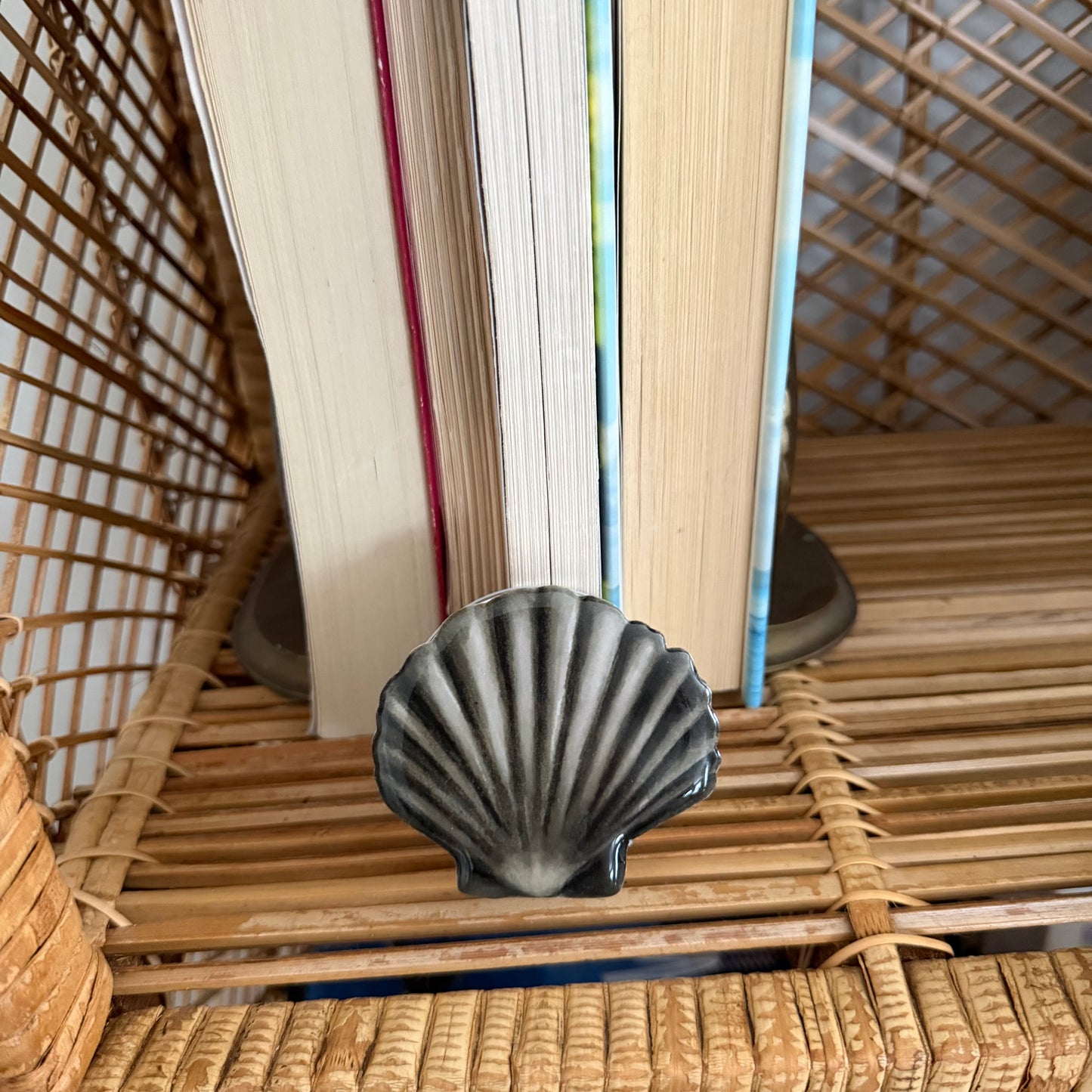 Decorative shell phone pop grip on a woven surface with books in the background