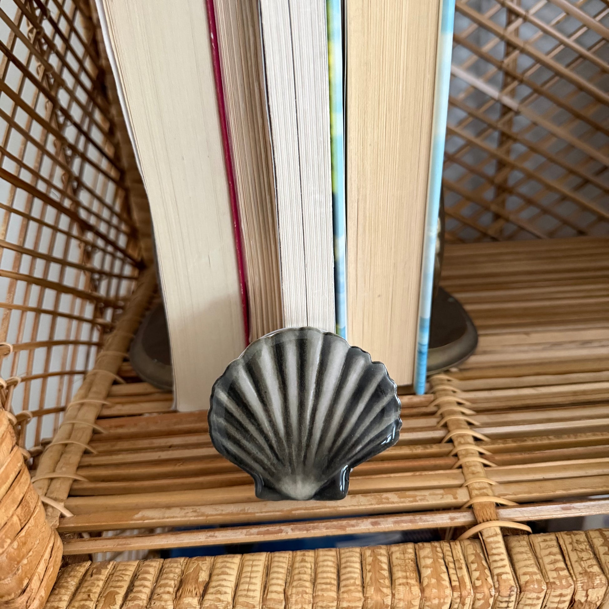 Decorative shell phone pop grip on a woven surface with books in the background