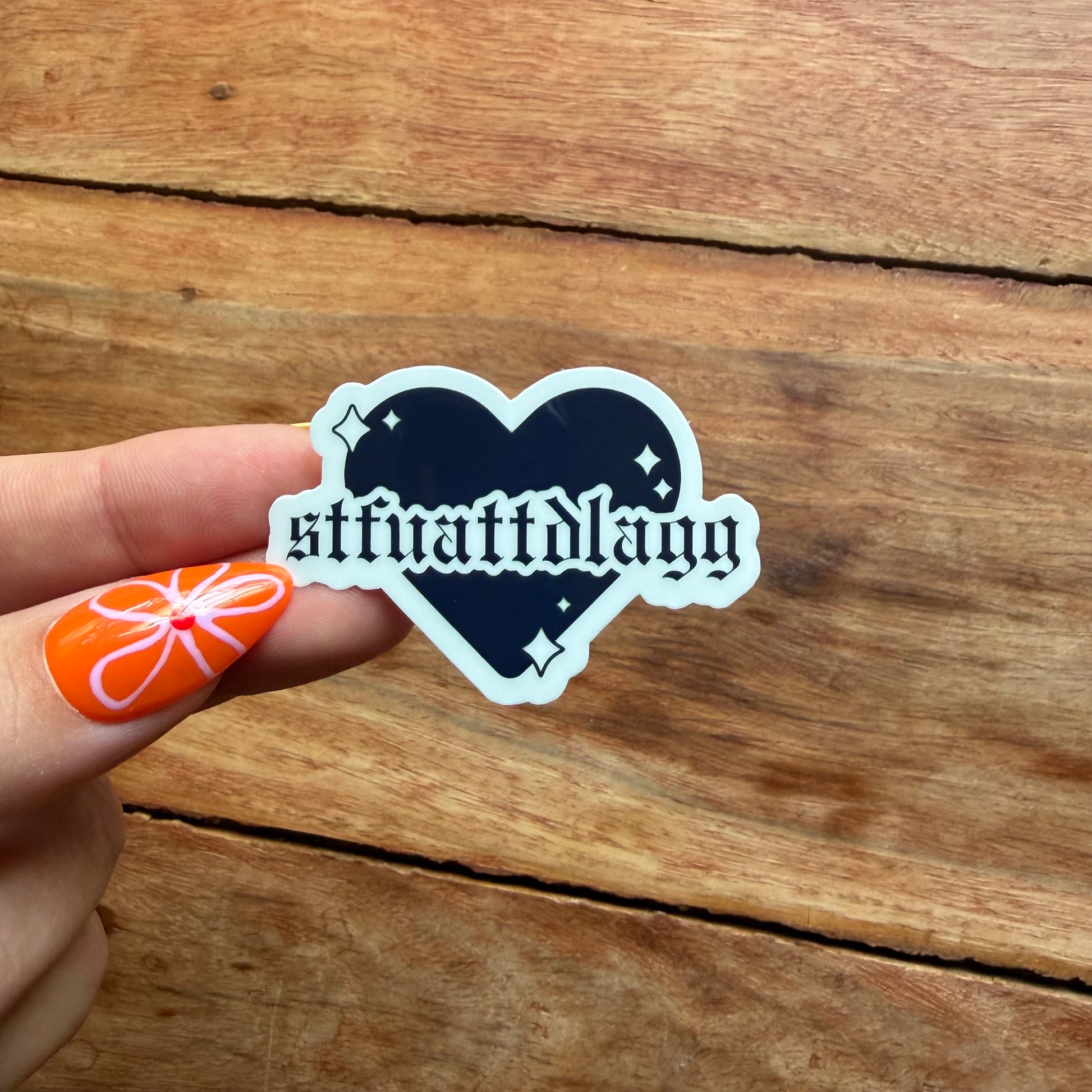 Heart-shaped sticker with text held by a hand on a wooden surface