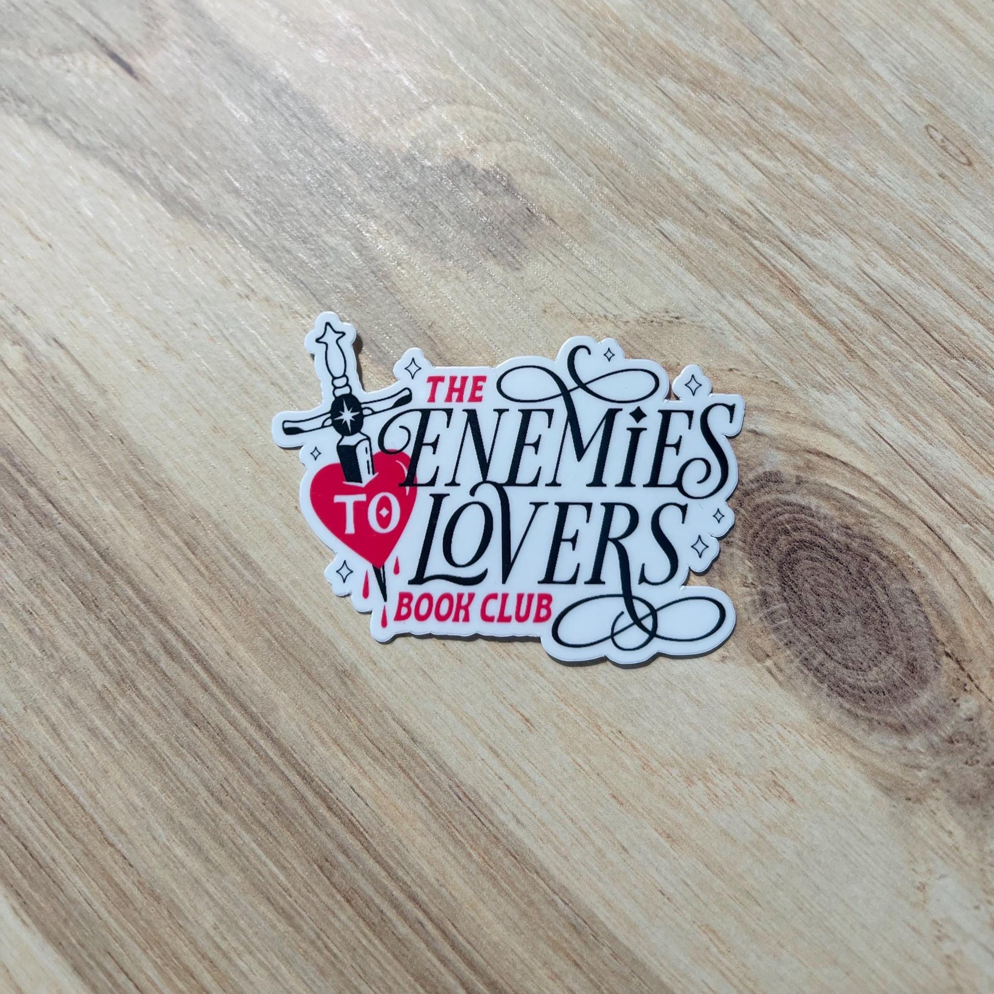 Sticker for 'The Enemies to Lovers Book Club' on a wooden surface